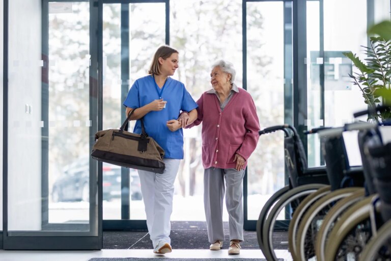 Nurse helping senior woman with bag, coming for planned surgery. Worried senior patient talking with nurse. Emotional support from healthcare workers for elderly woman.